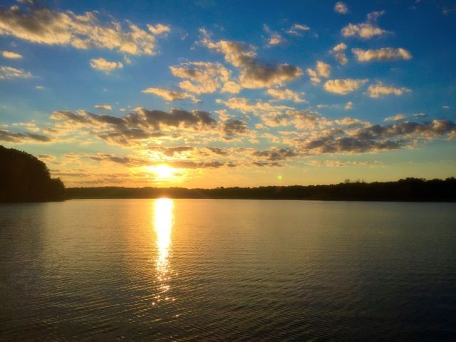 Sunset over a calm lake with golden reflections and scattered clouds in a blue sky