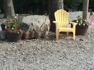 Yellow chair between flower pots beside a large rock on a gravel yard