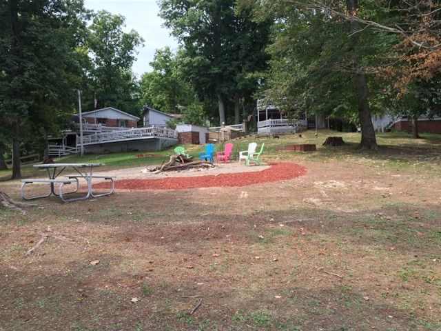 Playground with colorful chairs around a red sand play area in a grassy park near trees and houses