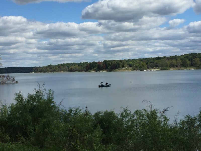 Lake scene with a small boat on calm water, green shoreline, and cloudy sky