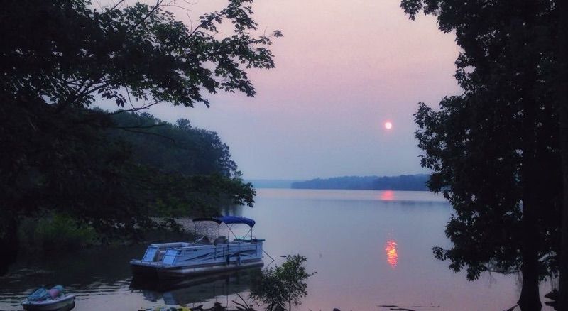 Dusk over a calm river with a small boat moored by the shore and a pink moon reflected in the water