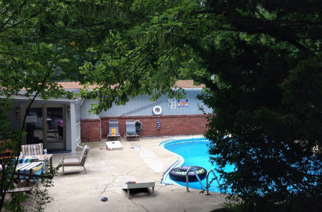 Backyard pool patio with lounge chairs, umbrella, and a blue swimming pool under trees