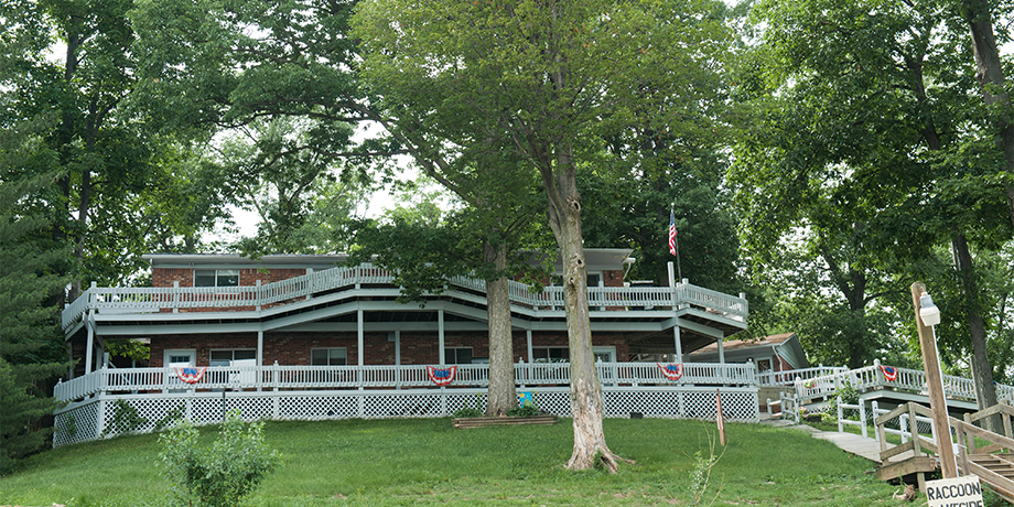 Large open-air pavilion with white railings and green roof surrounded by trees and a wooden deck