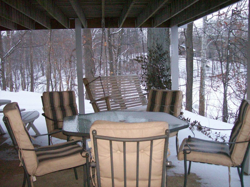 Covered patio with glass table and chairs overlooking a snowy wooded backyard