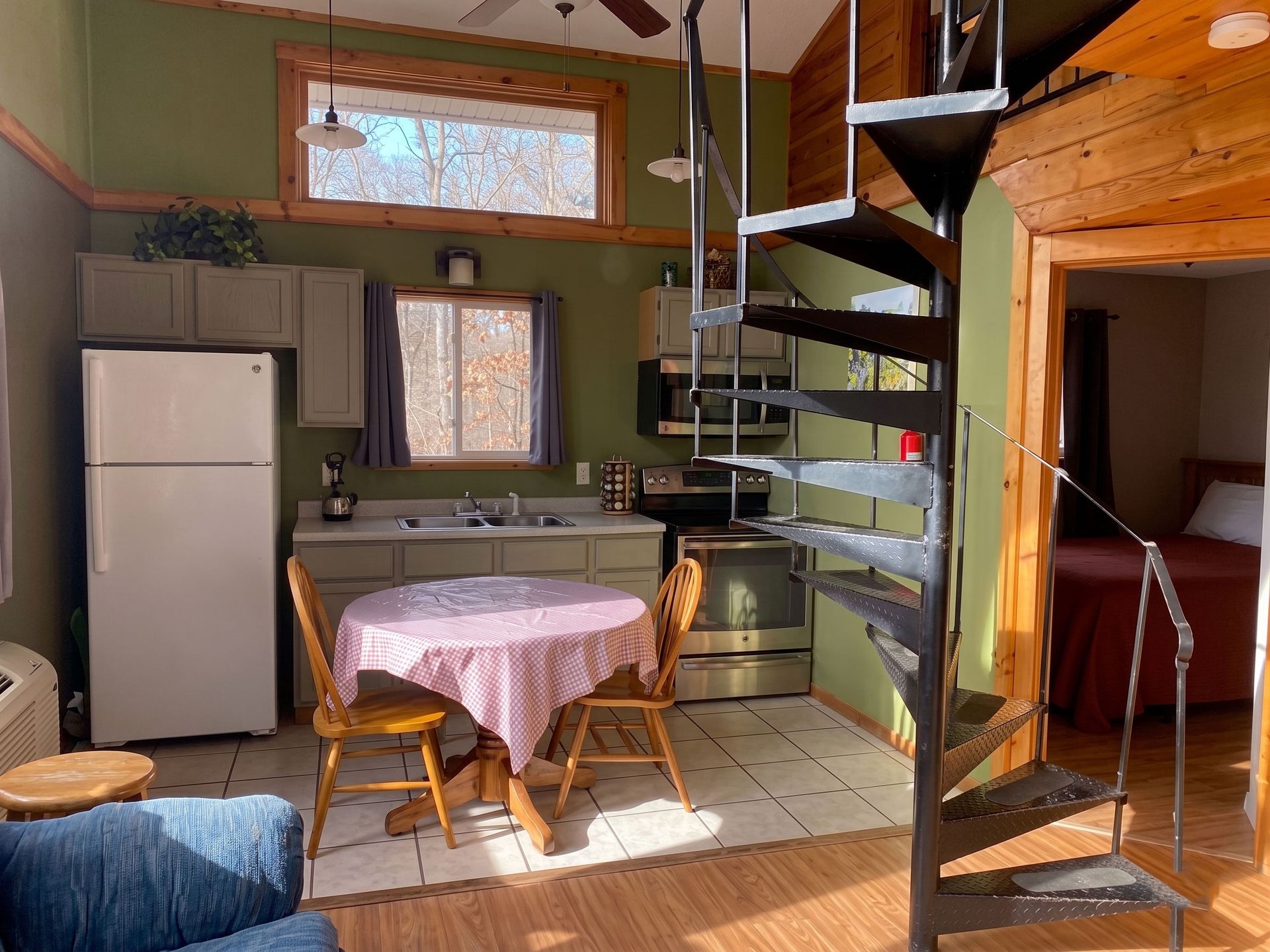 Cozy kitchen and living area with spiral staircase, table, fridge, and large windows