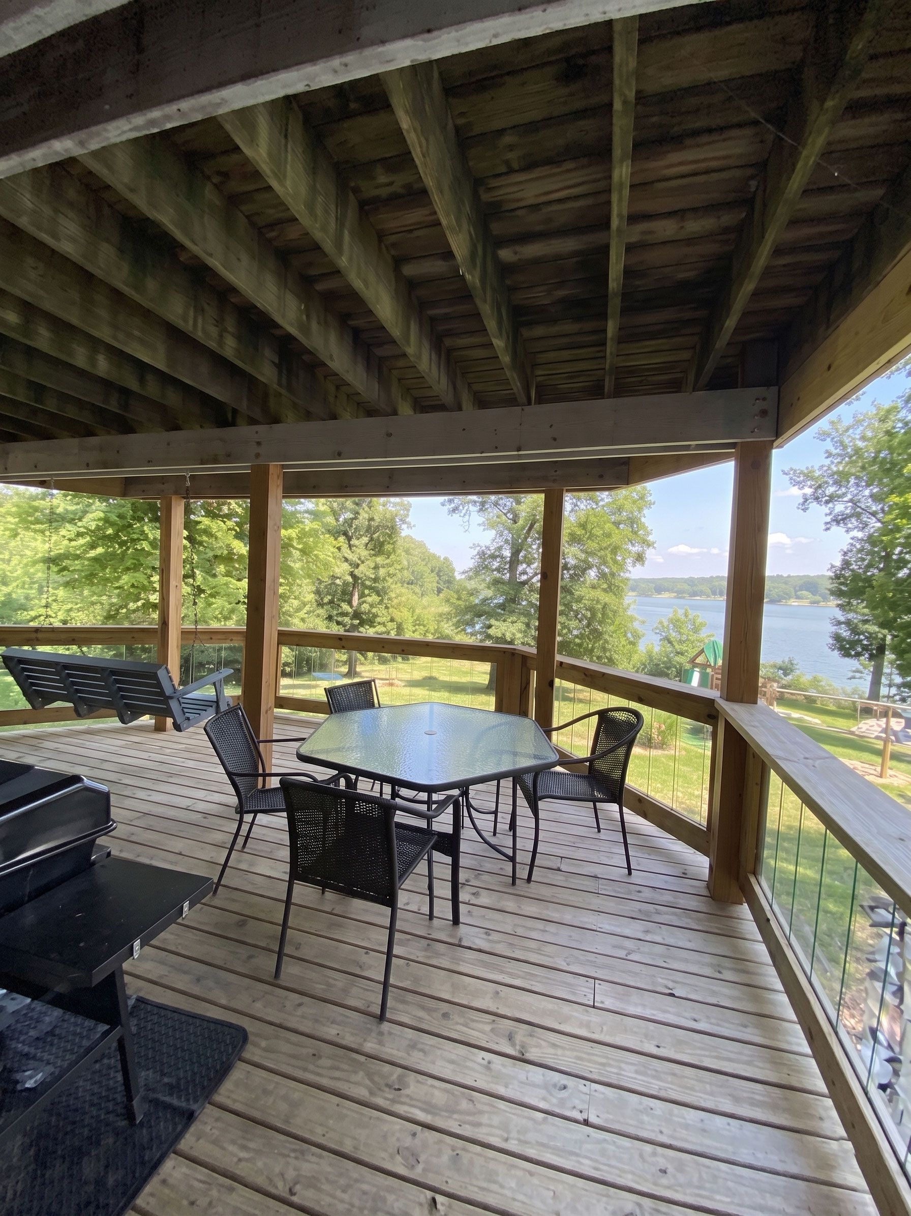 Covered wooden deck with table and chairs overlooking a wooded landscape and water.