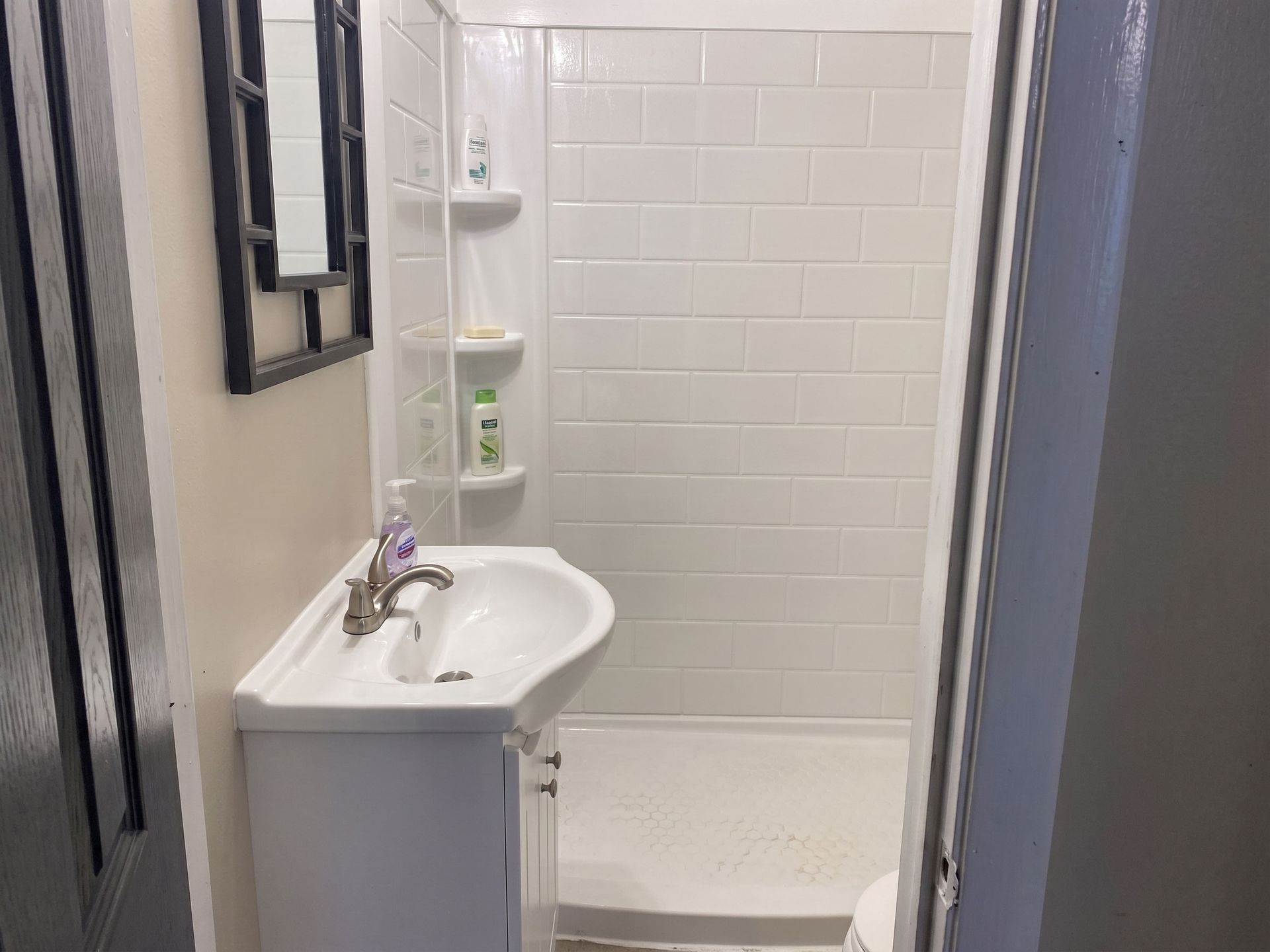 Small white bathroom with sink, mirror, and shower stall with tiled walls