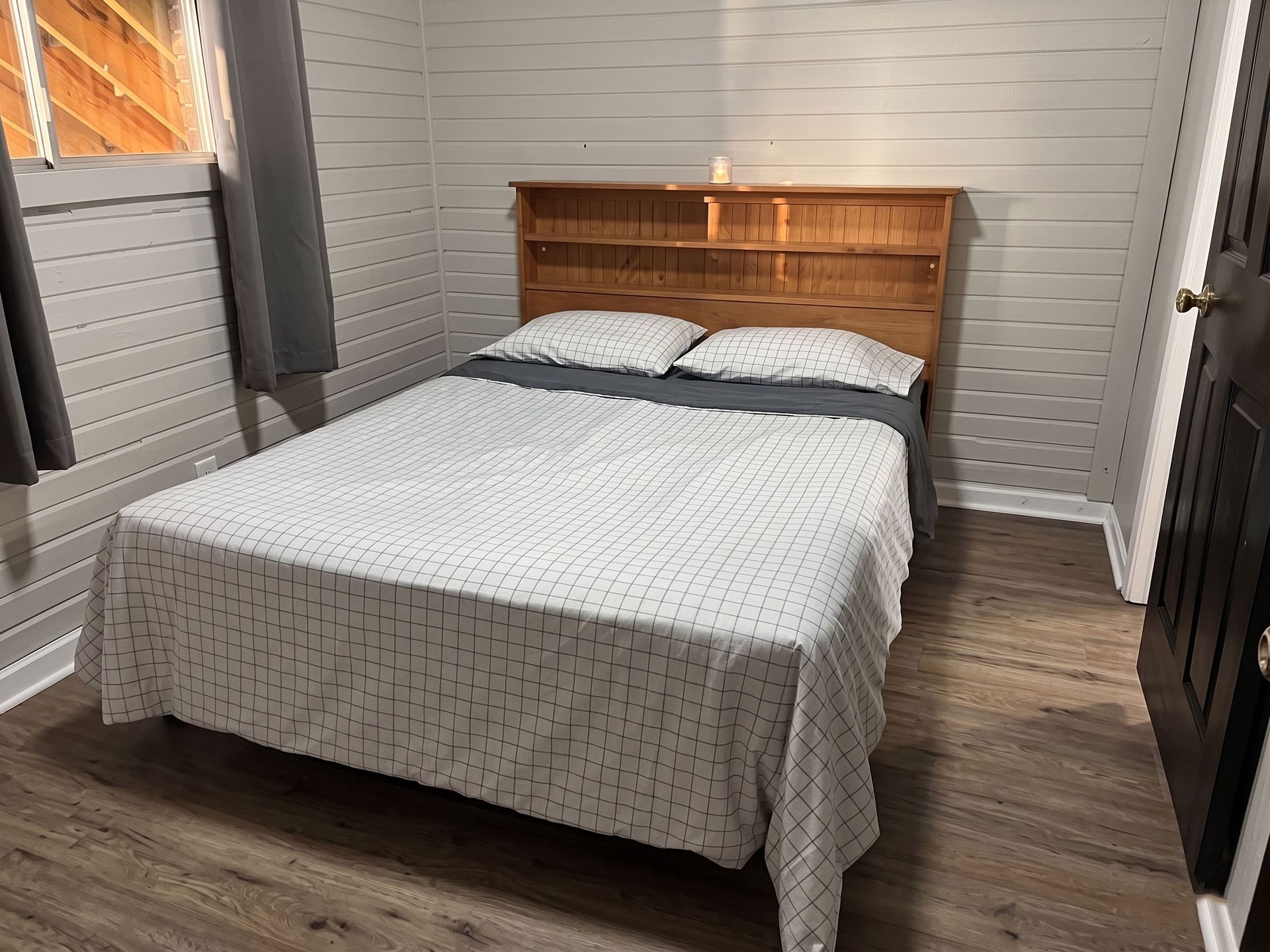 Small bedroom with a made bed, wooden headboard, gray walls, and wood-look flooring.