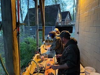 People working at a long table in a workshop or garage, using tools under bright lights.