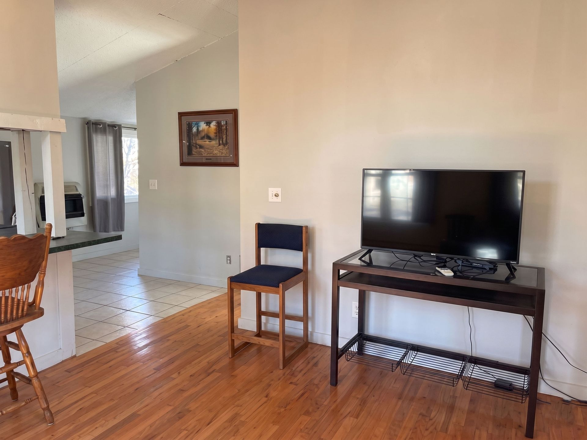 Empty living room with hardwood floor, TV on a stand, chair, and wall mirror near a doorway.
