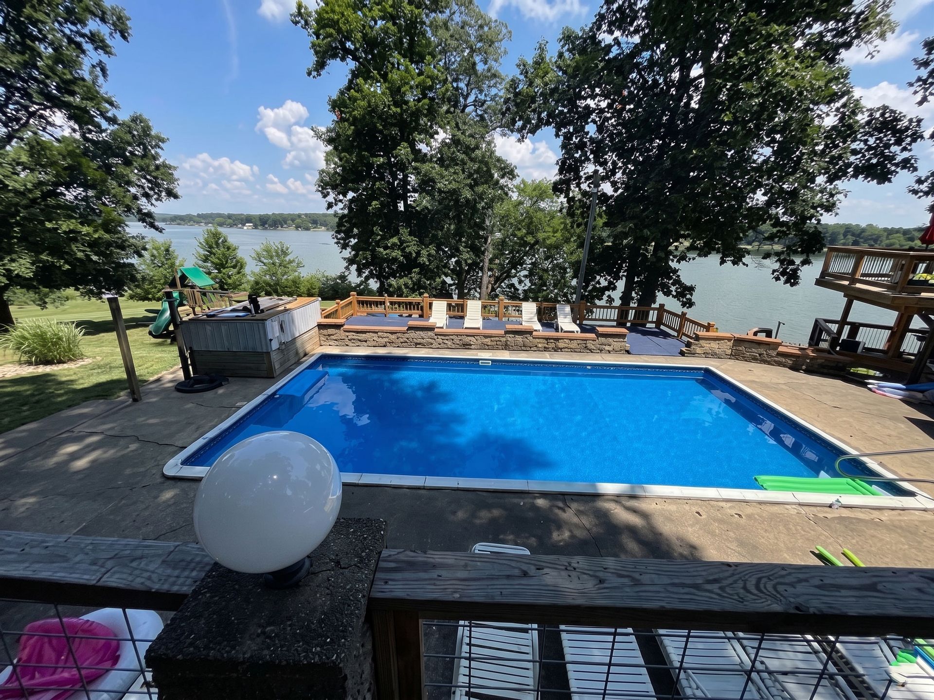Backyard pool with blue water, lounge chairs, trees, and a lake view beyond the deck.