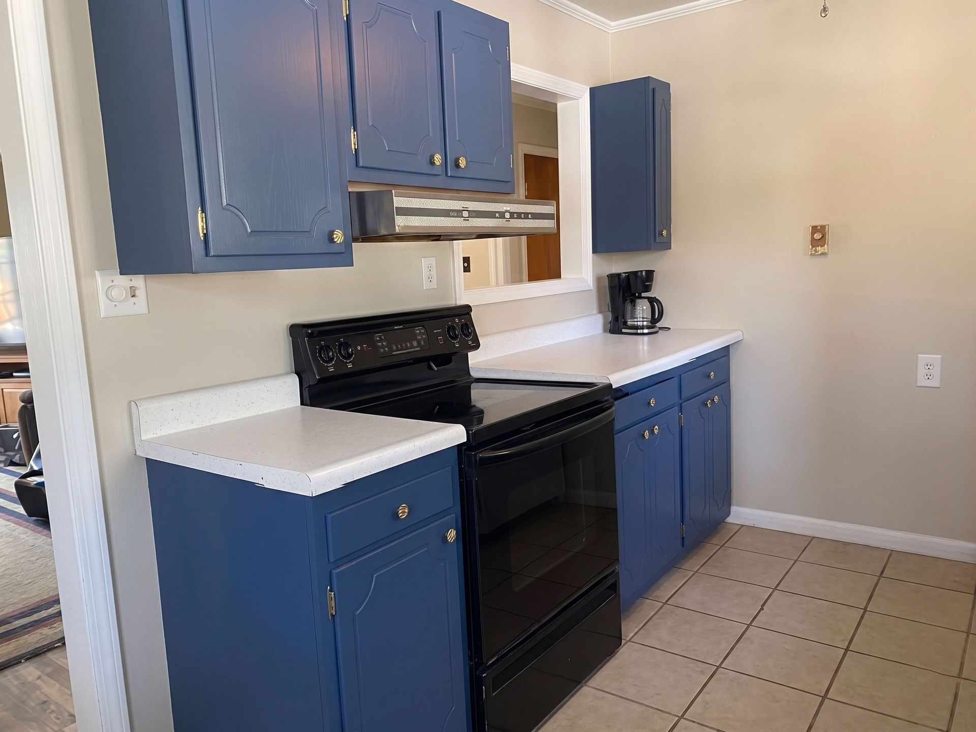 Blue kitchen cabinets, black stove, white countertops, and beige tiled floor in a small kitchen.