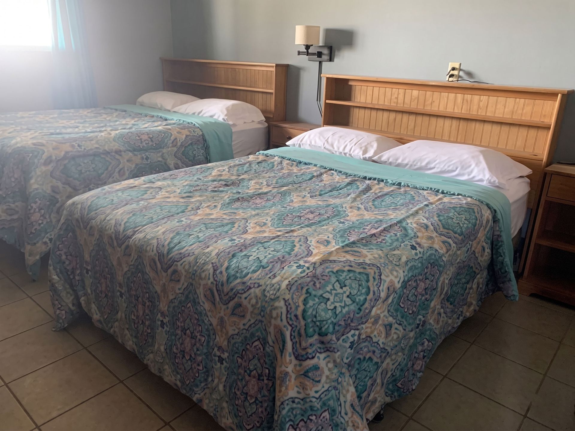 Two neatly made beds with patterned blue bedspreads in a simple tiled hotel room