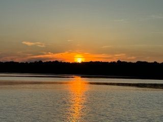 Sunset over a calm lake, with orange reflections on the water and a dark tree-lined horizon.