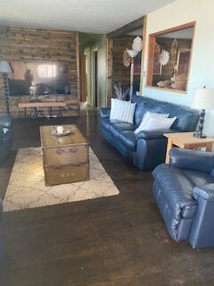 Living room with leather seating, coffee table, and stone fireplace with TV on the wall