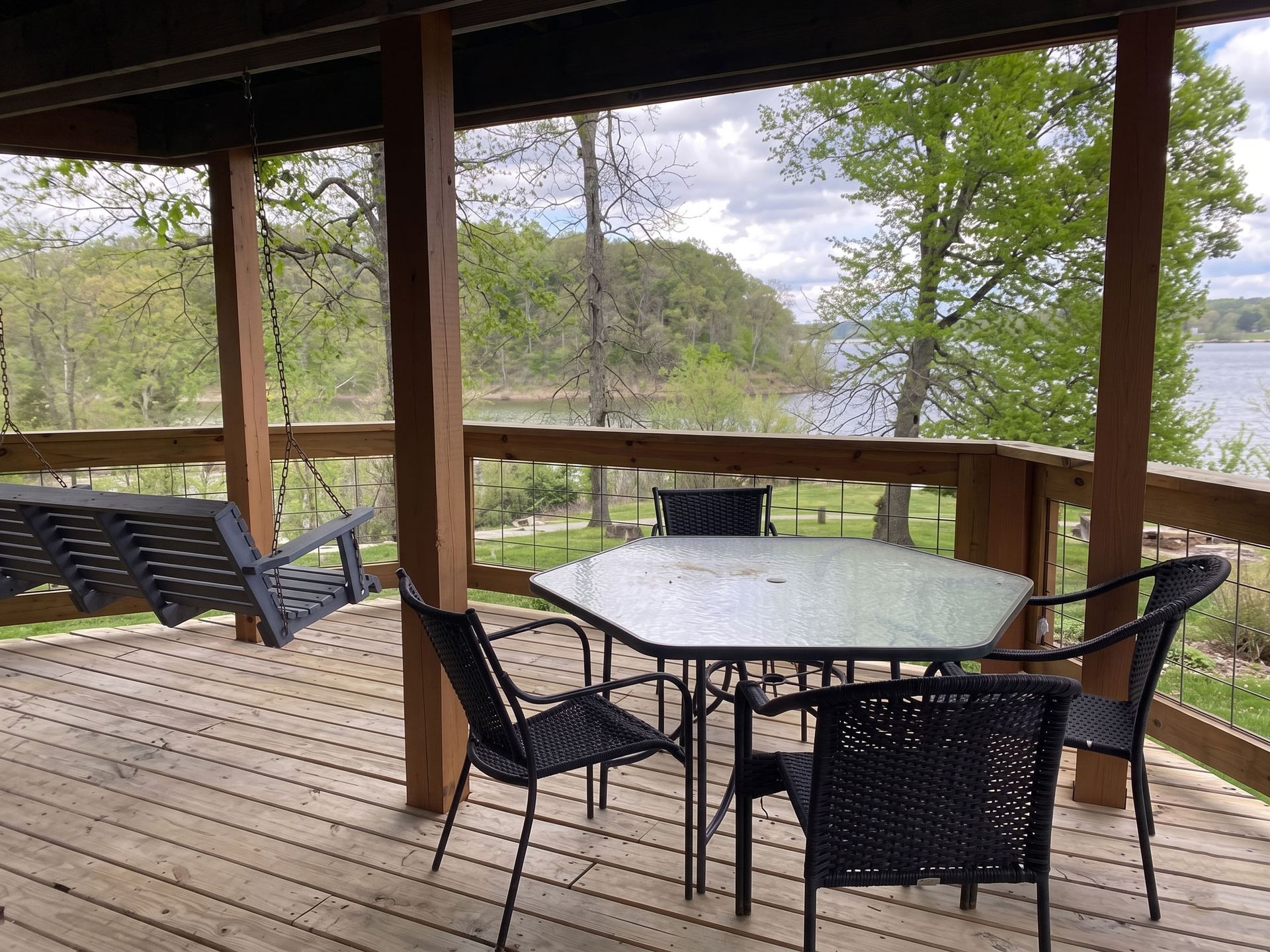 Wooden porch with patio table and chairs overlooking a lake and trees