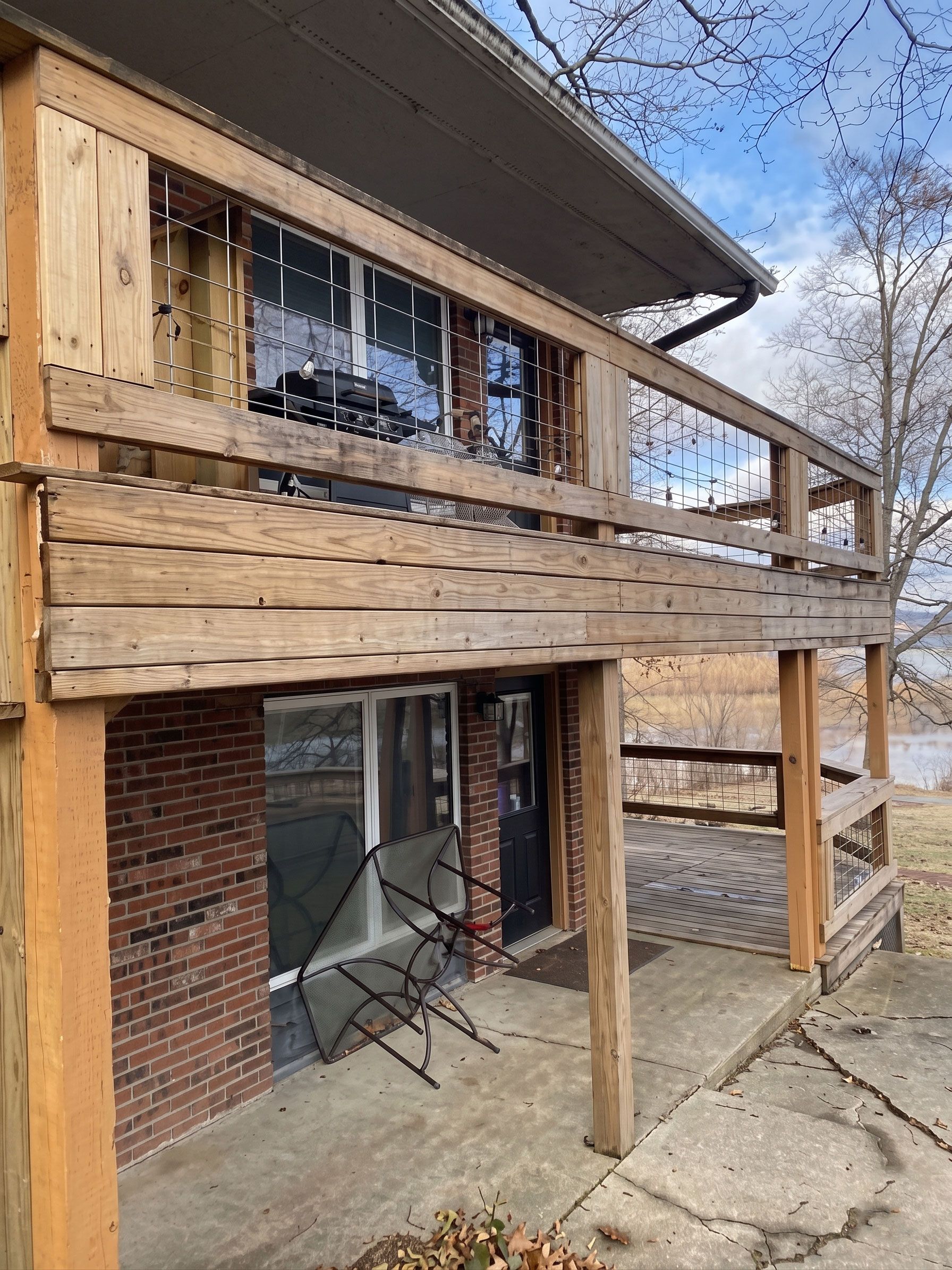 Weathered wooden deck and upper balcony on a rustic house exterior with brick and glass doors below.