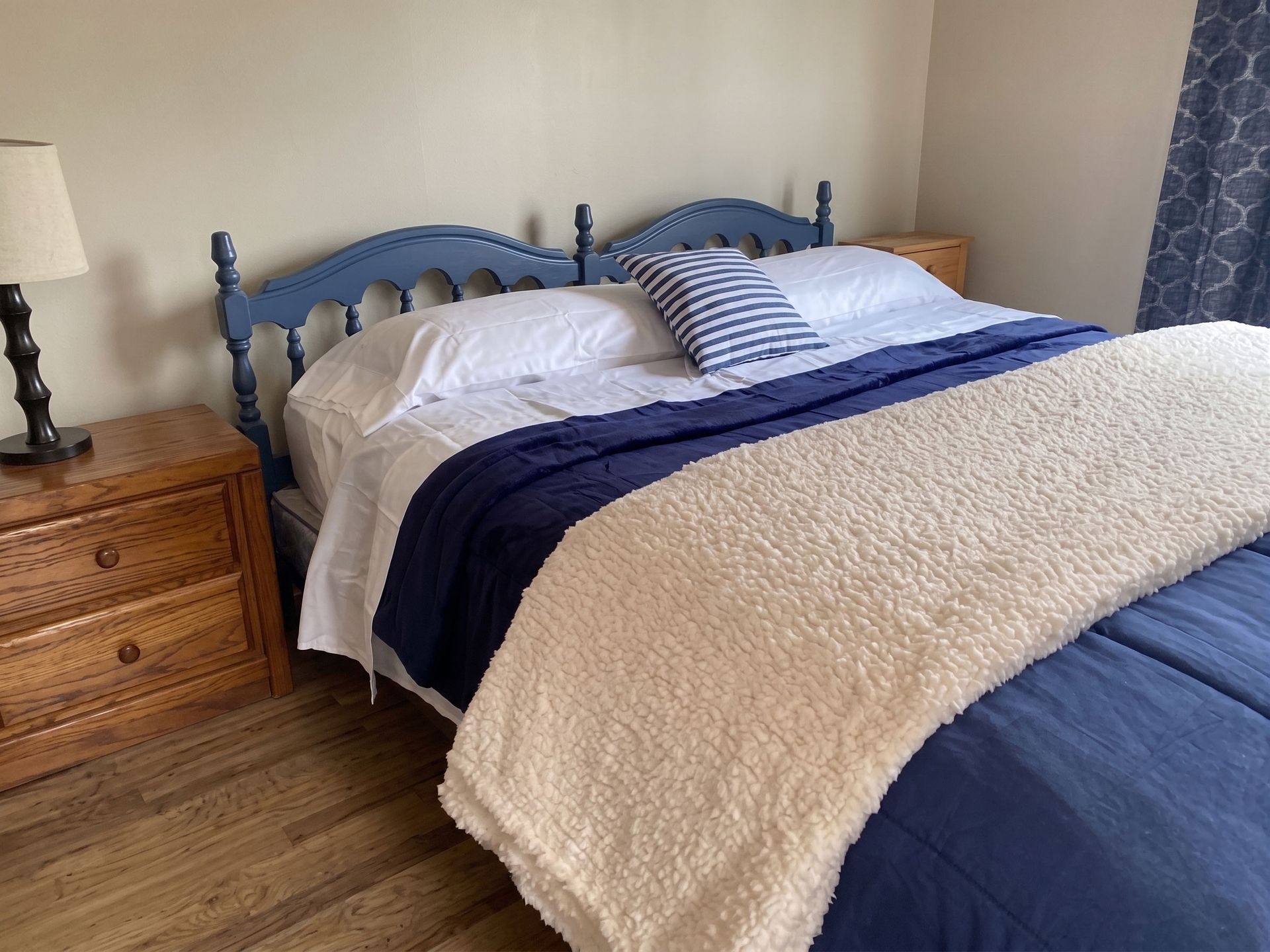 Bedroom with blue bed frame, white bedding, striped pillows, and wooden nightstands on a wood floor