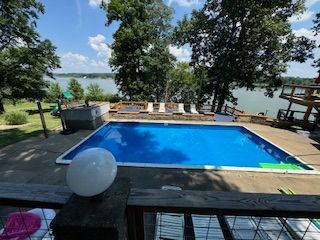 Backyard pool with blue water, trees, deck chairs, and a lake view beyond the railing