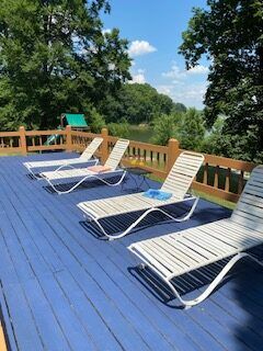 Blue deck with white lounge chairs overlooking a green, wooded landscape under a sunny sky