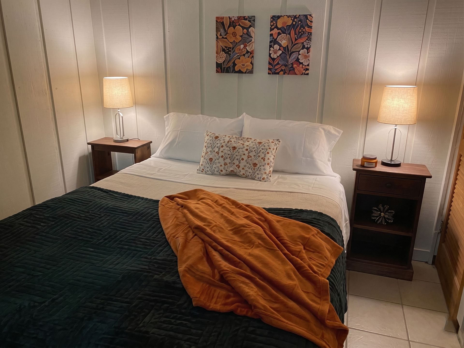 Cozy bedroom with a made bed, bedside lamps, and framed artwork above the headboard.