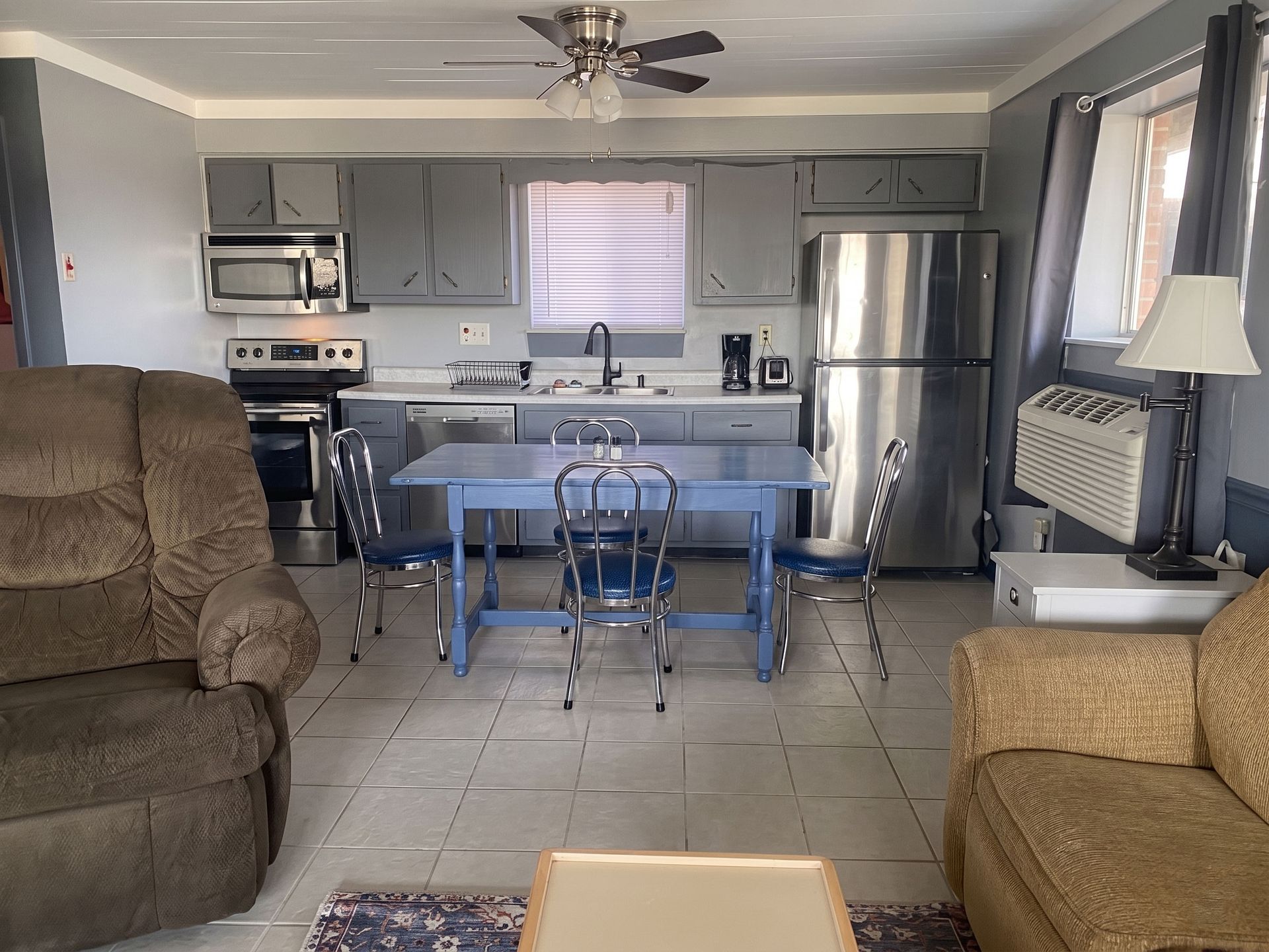 Living room open to kitchen with gray cabinets, stainless fridge, blue table, and brown sofas