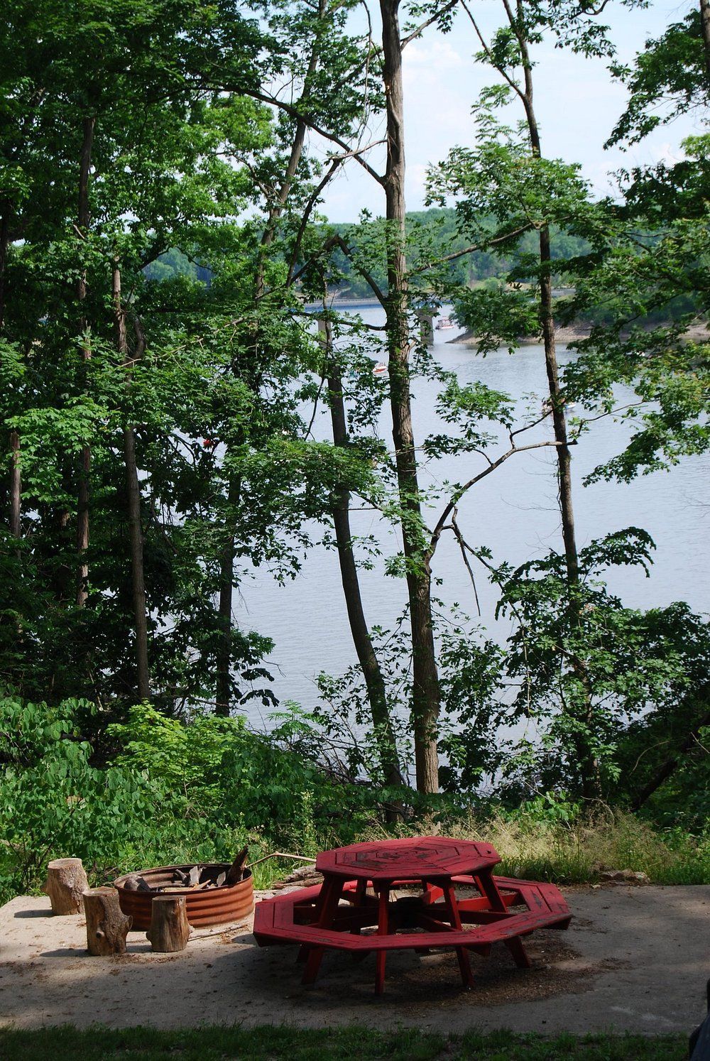 Red picnic table and benches in a wooded park by a lake