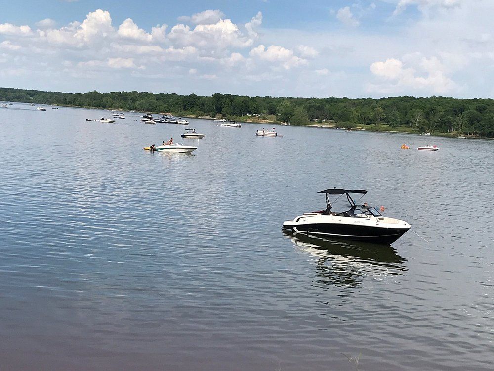 Several small boats on a calm lake, with a white-and-black motorboat in the foreground and a tree-lined shore beyond.