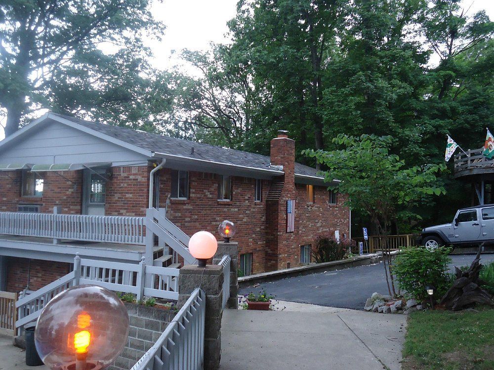 Brick house with white ramp and steps, glowing garden lights, and a parked SUV under trees.