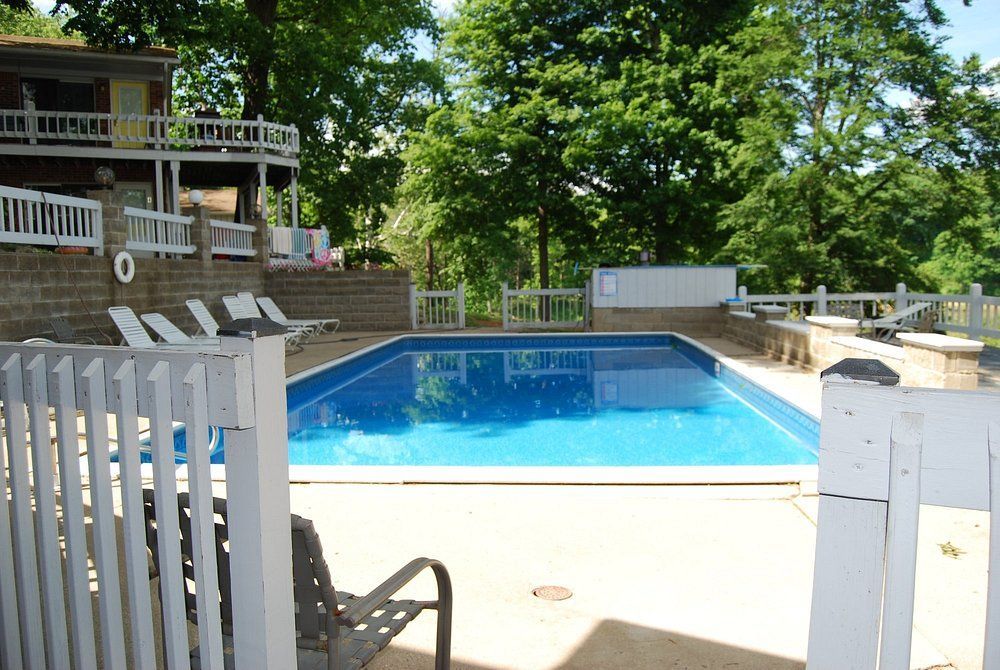 Backyard swimming pool with blue water, white fence, and lounge chairs beside a house