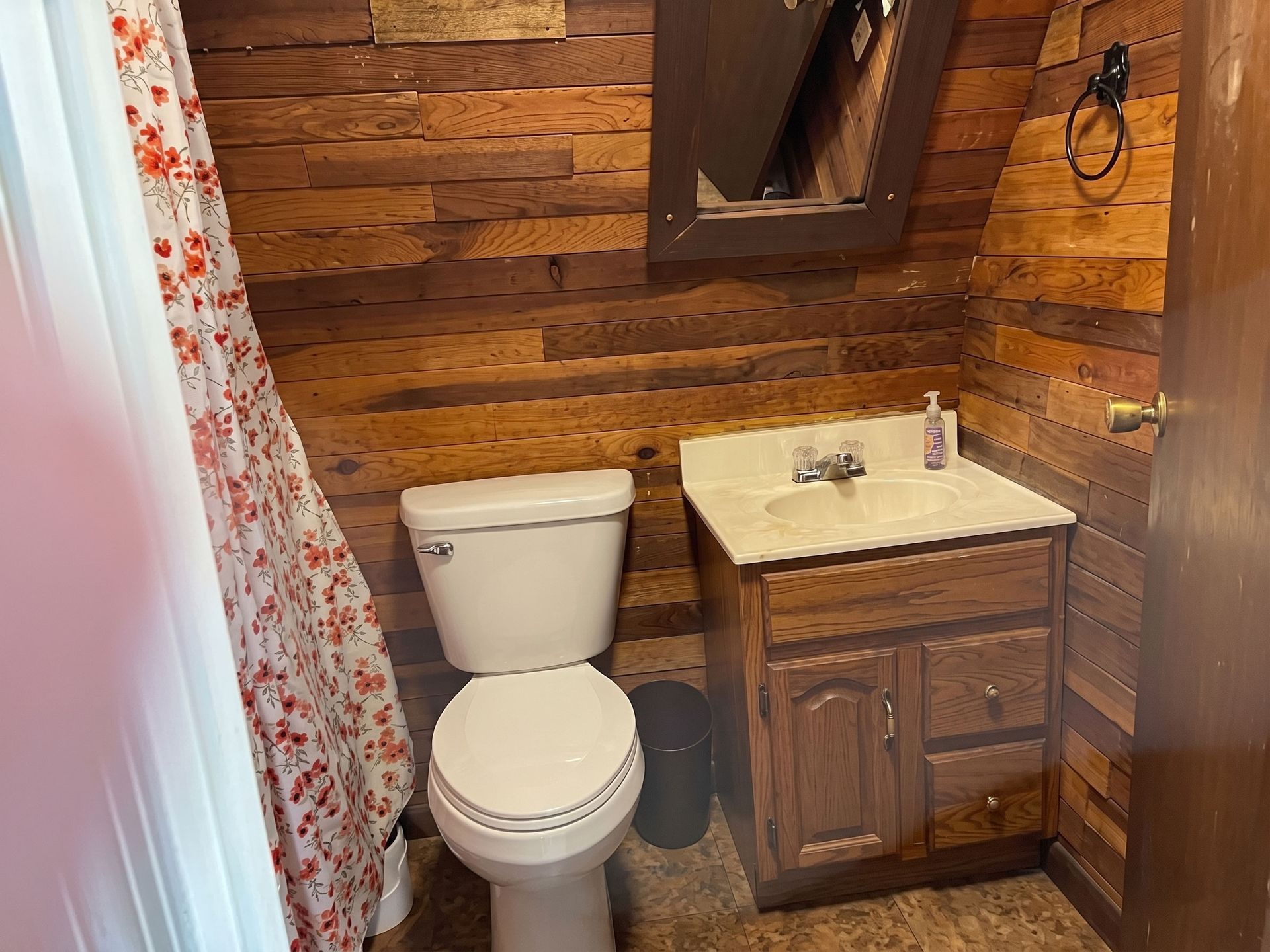 Small rustic bathroom with a toilet, wood-paneled walls, and a marble sink vanity.