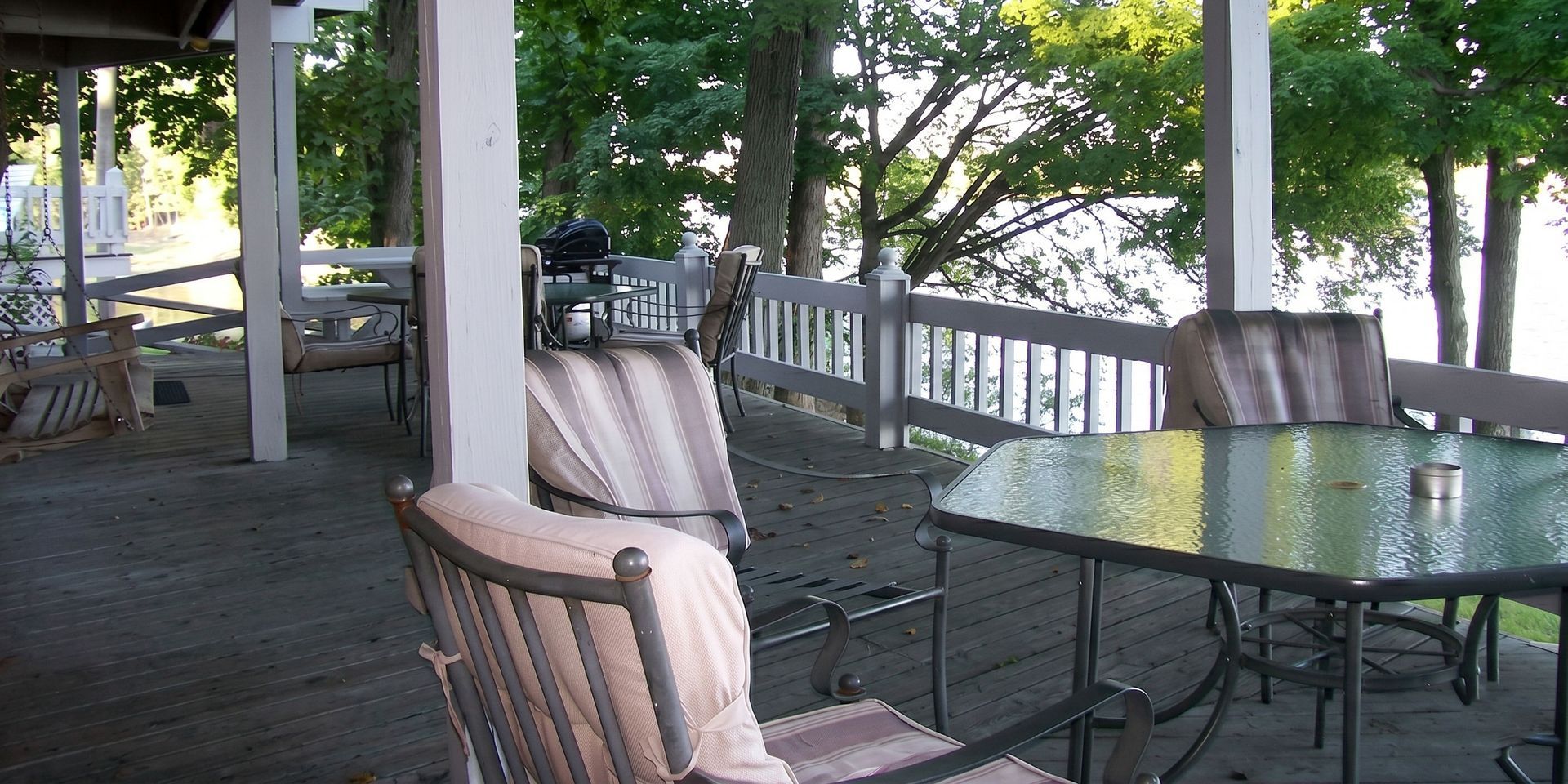 Covered porch with wicker chairs and a glass-top table overlooking trees and water
