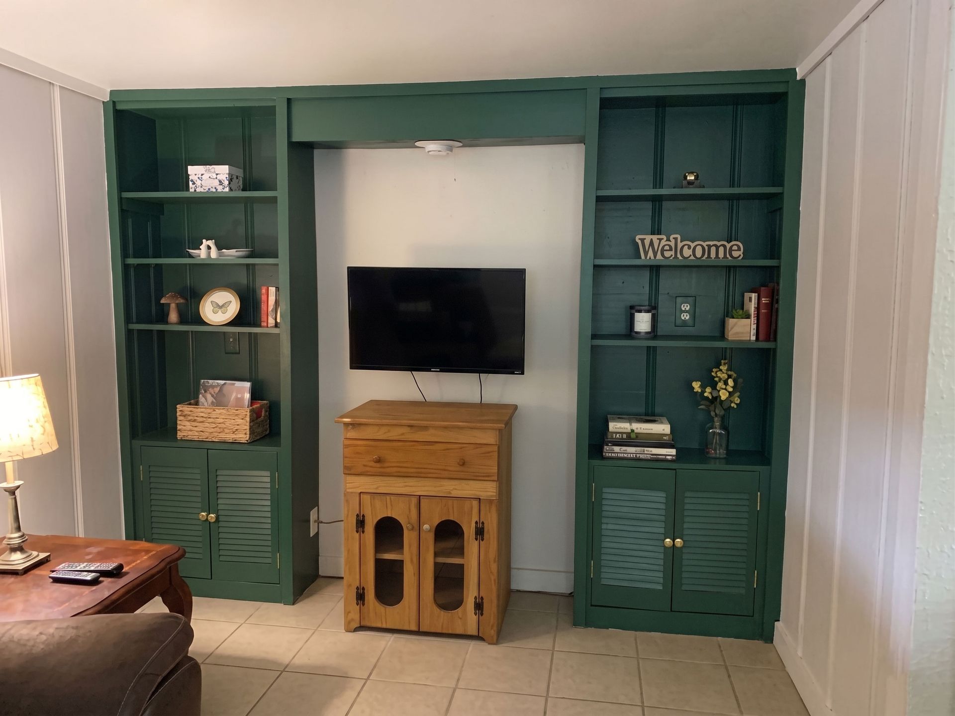 Living room wall with built-in green shelves, a wall-mounted TV, and a small wooden cabinet underneath