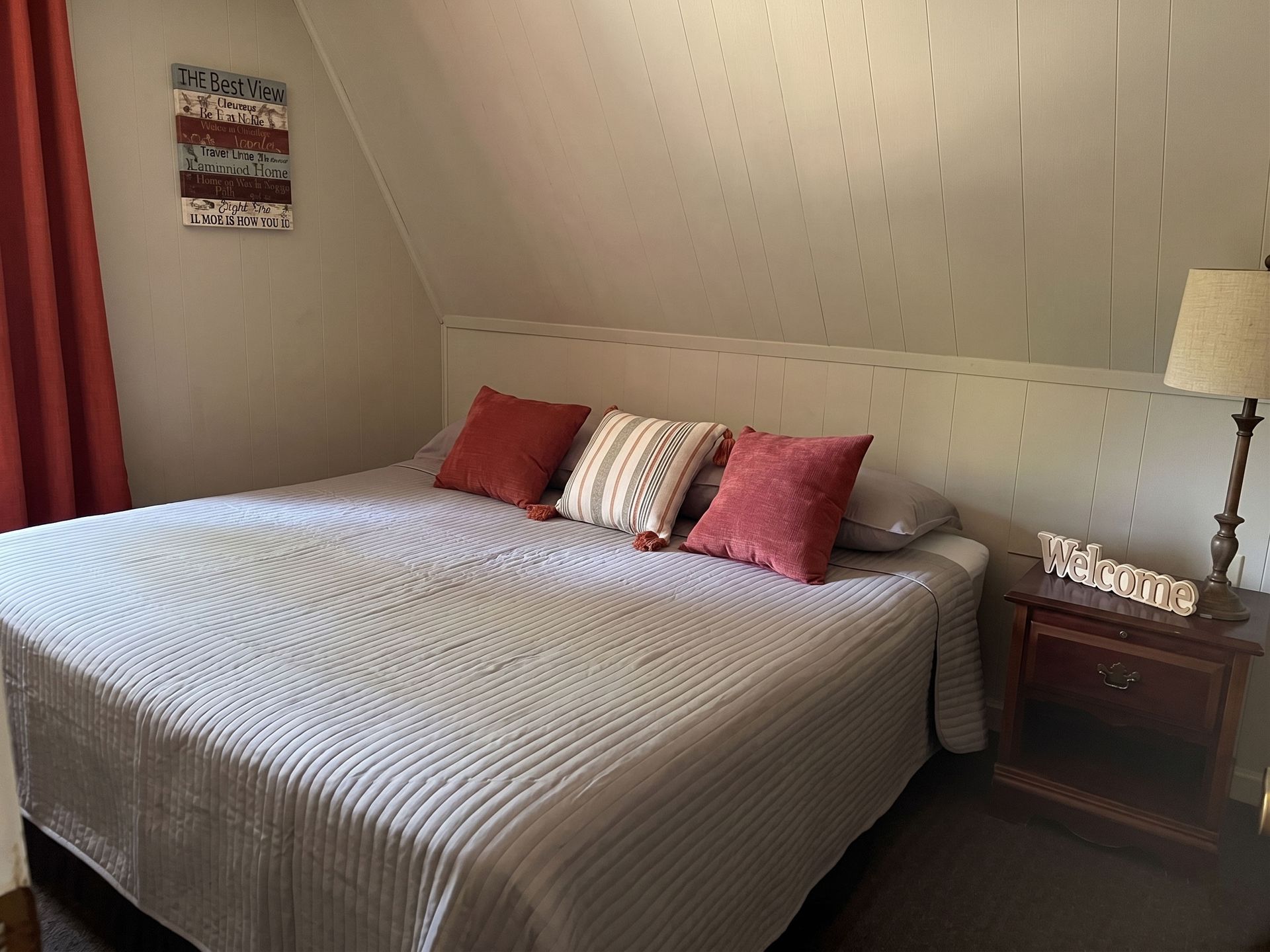 Cozy attic bedroom with a large bed, striped bedding, red pillows, bedside table, and lamp