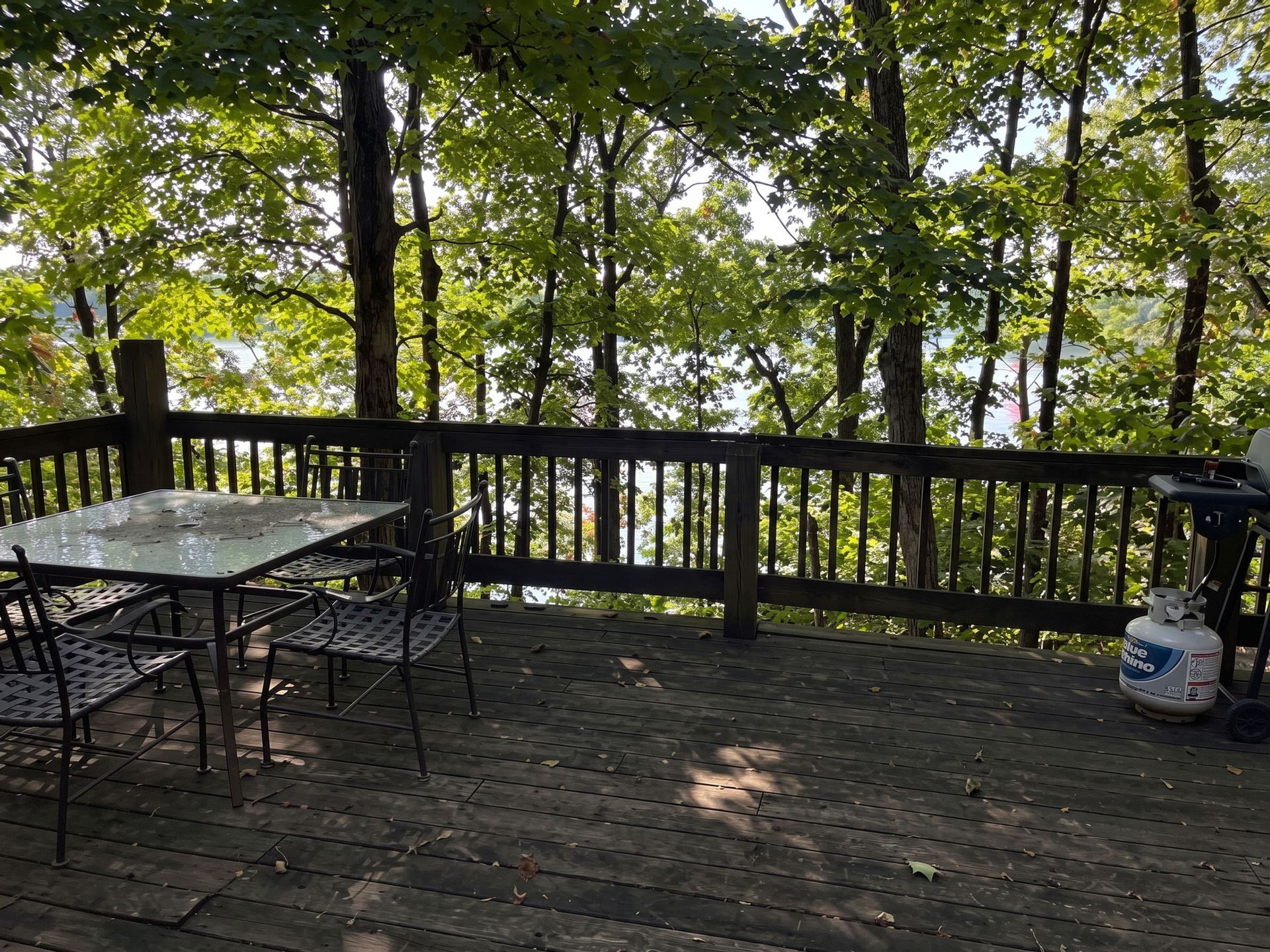 Wooden deck with railing and patio table set overlooking a wooded area, with a propane tank on the right.