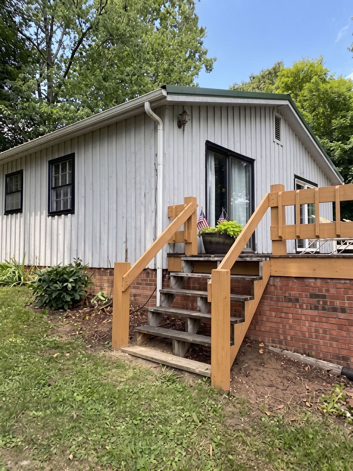 White house with small porch and wooden stairs, surrounded by trees and grass outdoors
