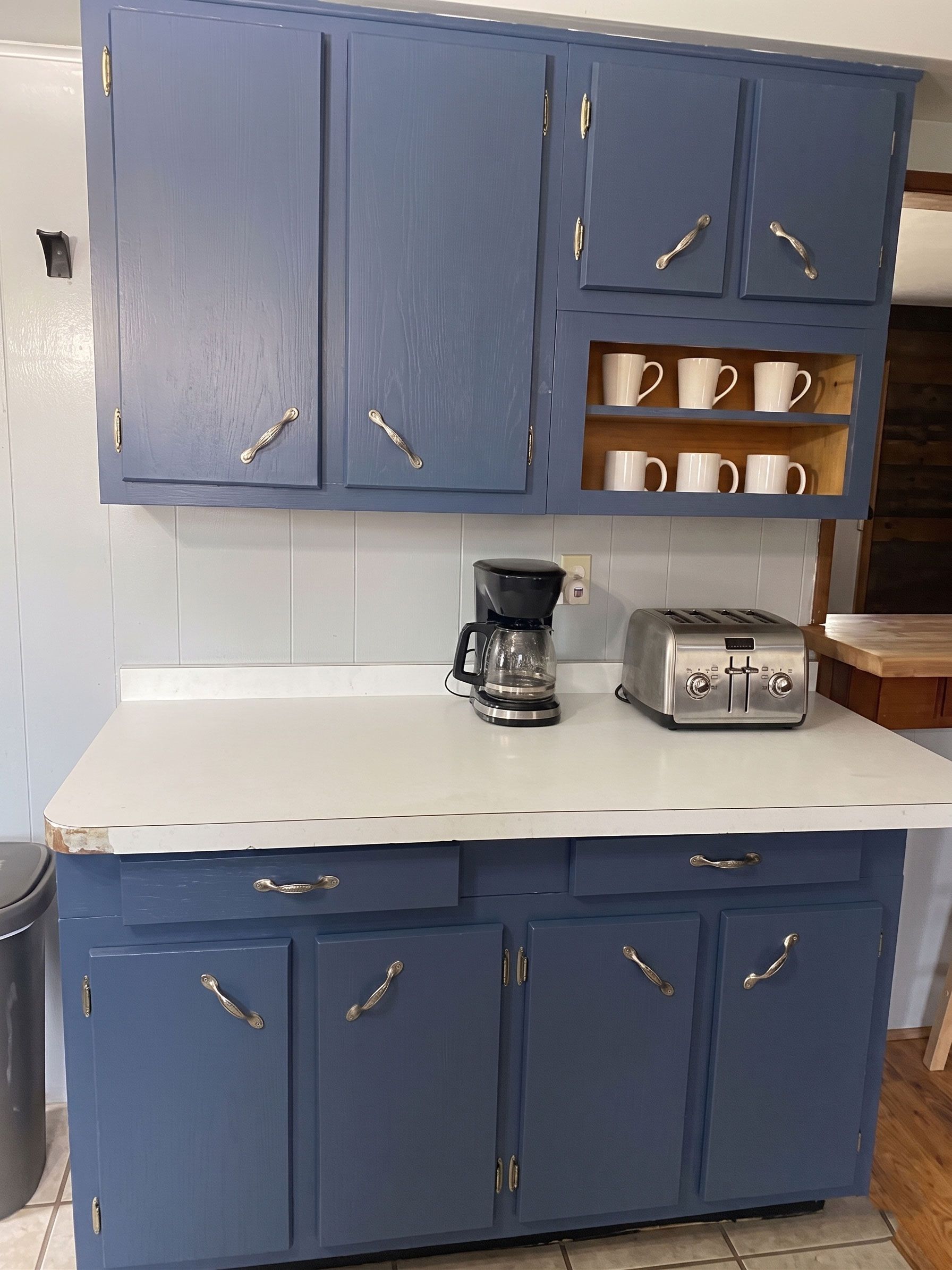 Blue kitchen cabinets with white countertop, coffee maker, toaster, and mugs