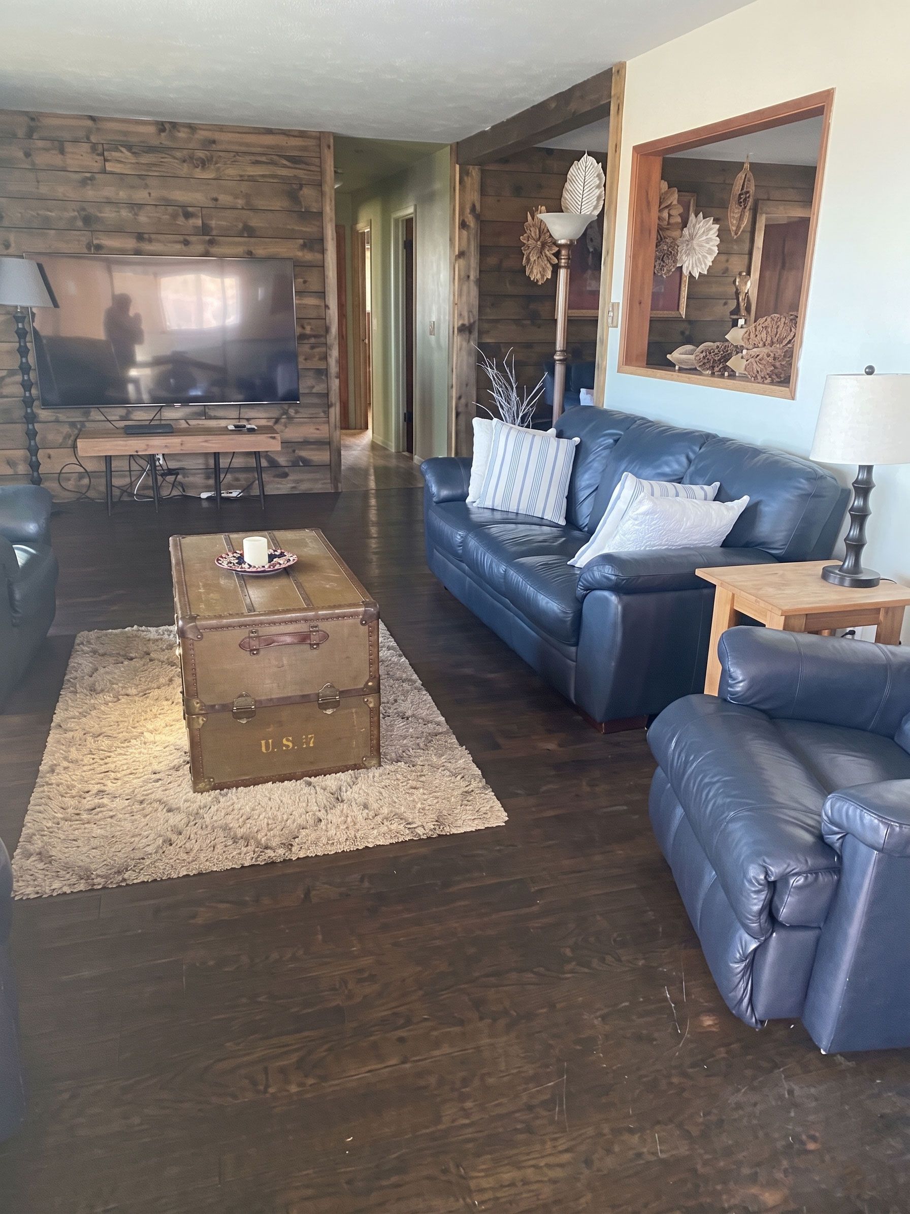 Cozy living room with leather sofas, stone TV wall, and wooden trunk coffee table on a rug.