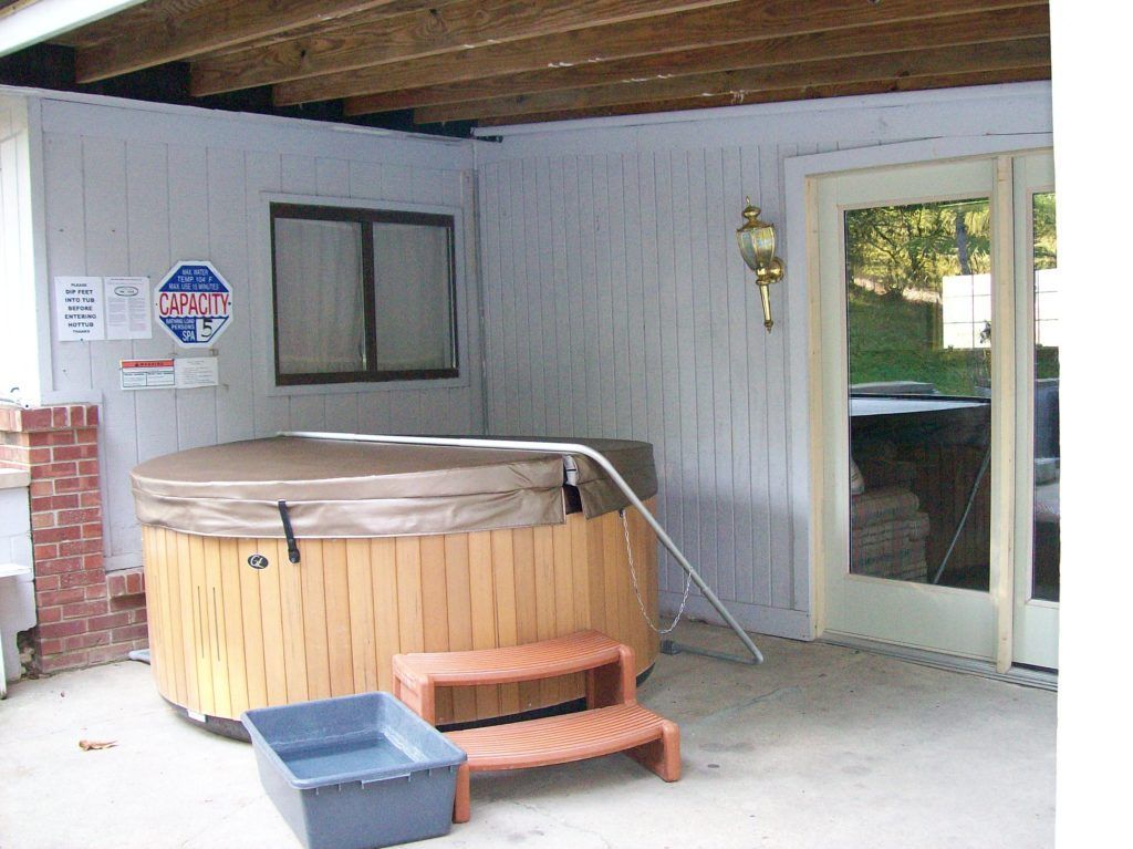 Covered patio with a round hot tub, small steps, storage bins, and a sliding glass door leading inside