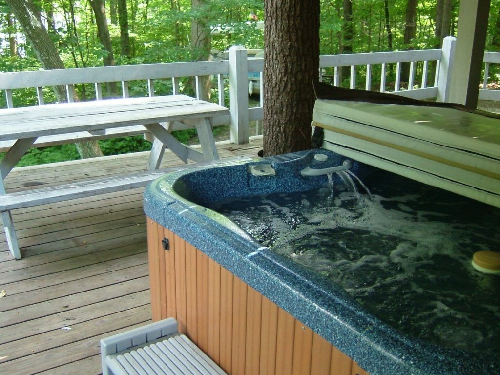 Outdoor hot tub on a wooden deck beside a picnic table in a wooded area
