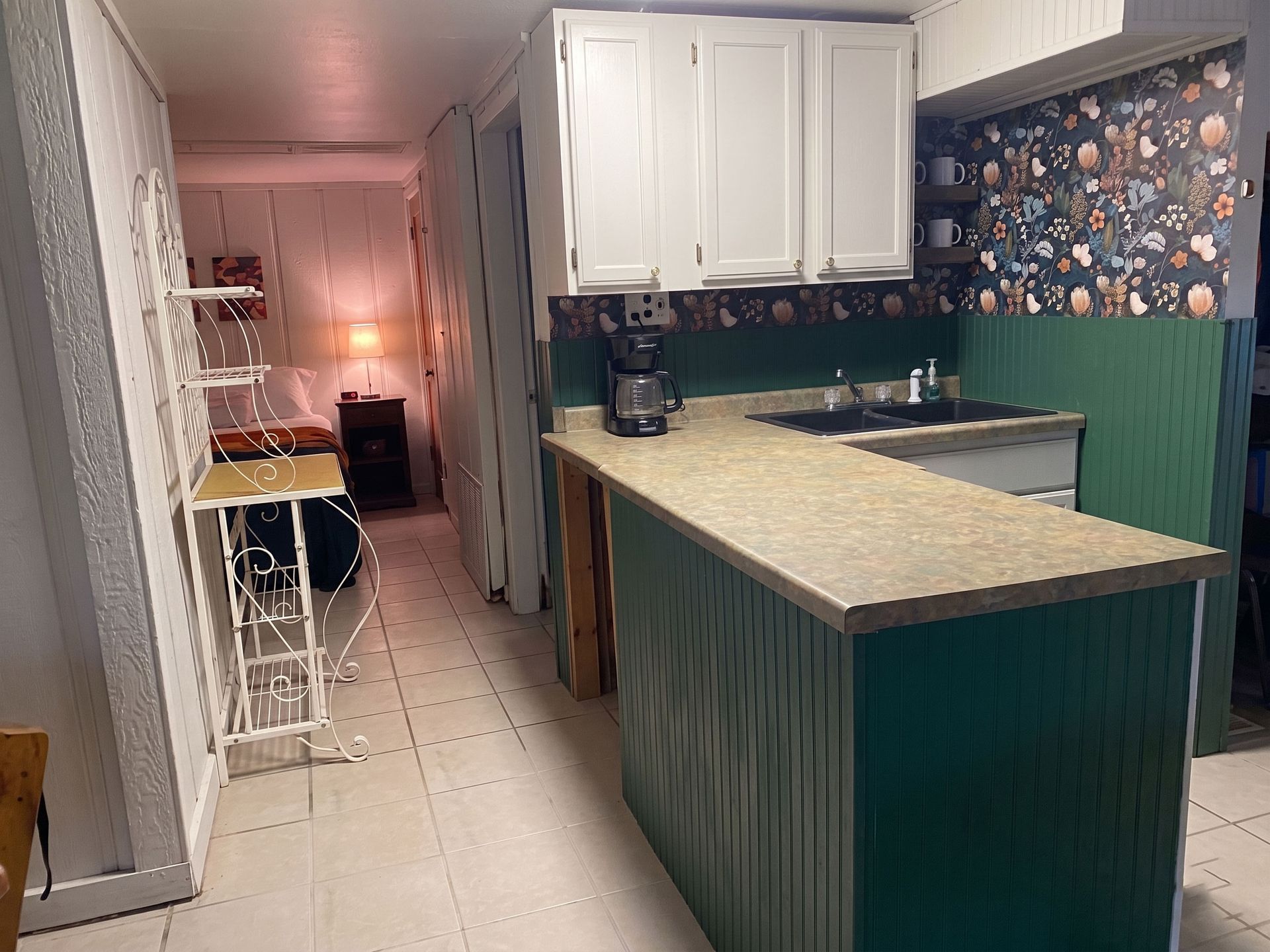 Narrow kitchen with white cabinets, green island, and a small dining area in the background.