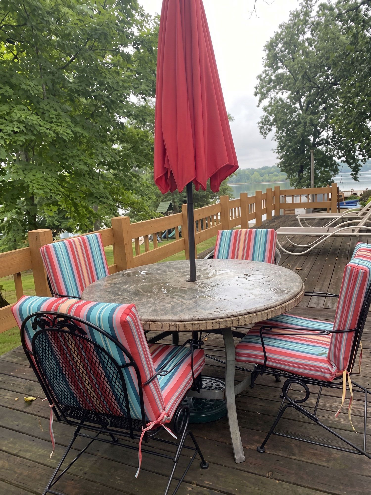 Patio table with striped chairs and a red umbrella on a wooden deck surrounded by trees