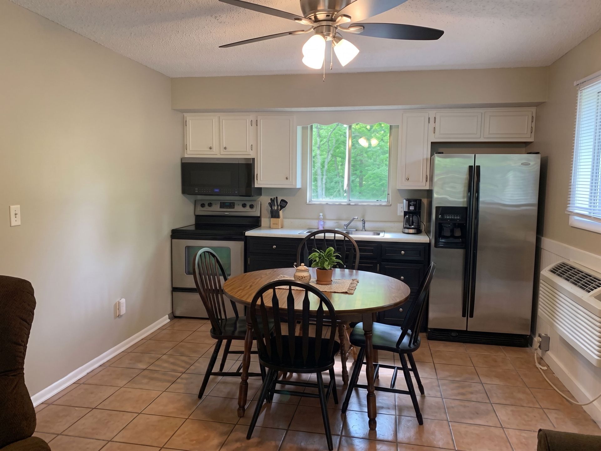 Small kitchen with white cabinets, black appliances, round table, and chairs on a tiled floor.