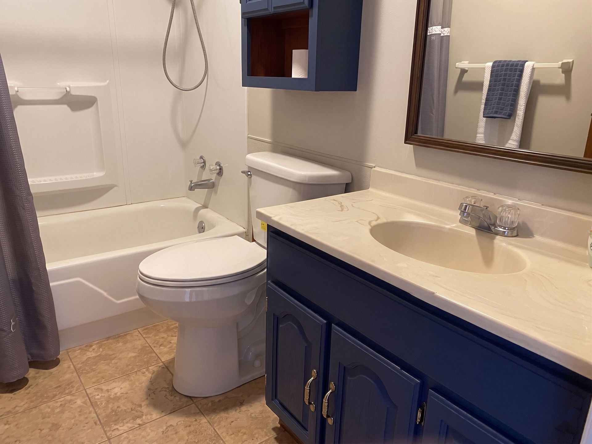 Small bathroom with tub, toilet, and navy vanity with sink and mirror.