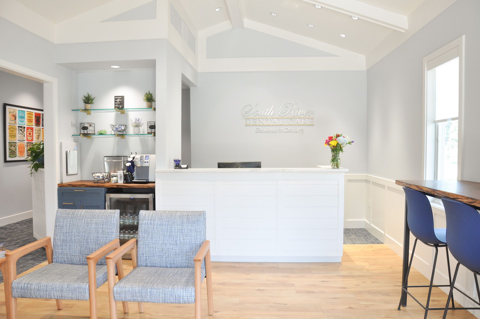 Reception area with white desk, blue chairs, wooden floor, and a colorful floral arrangement.