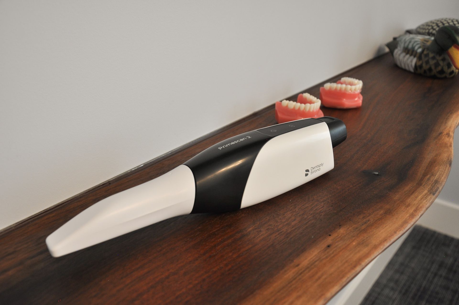 Digital dental scanner on a wooden shelf next to two sets of dental models.