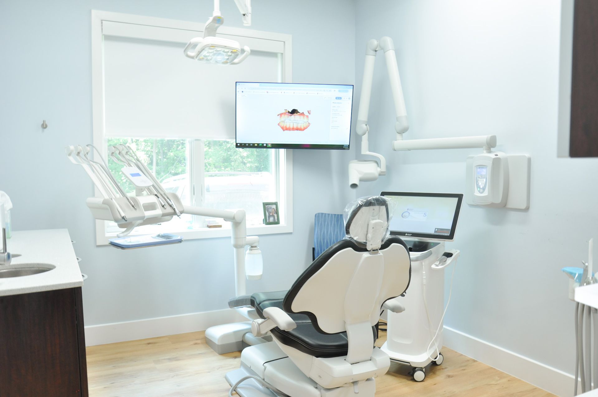 Dental office interior with chair, computer screen displaying teeth, and equipment. Light blue walls, window.