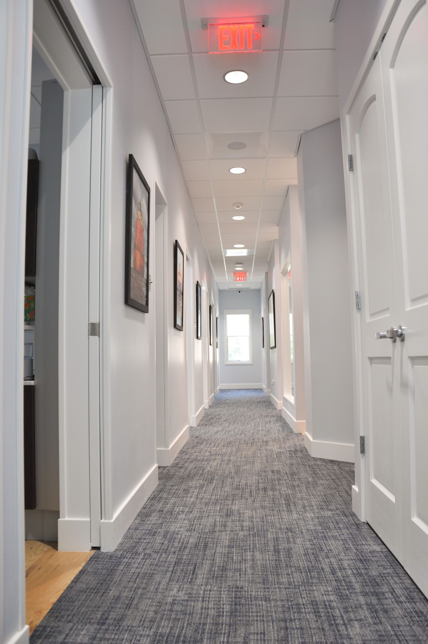 Narrow, long hallway with white walls, doors, and a patterned carpet.