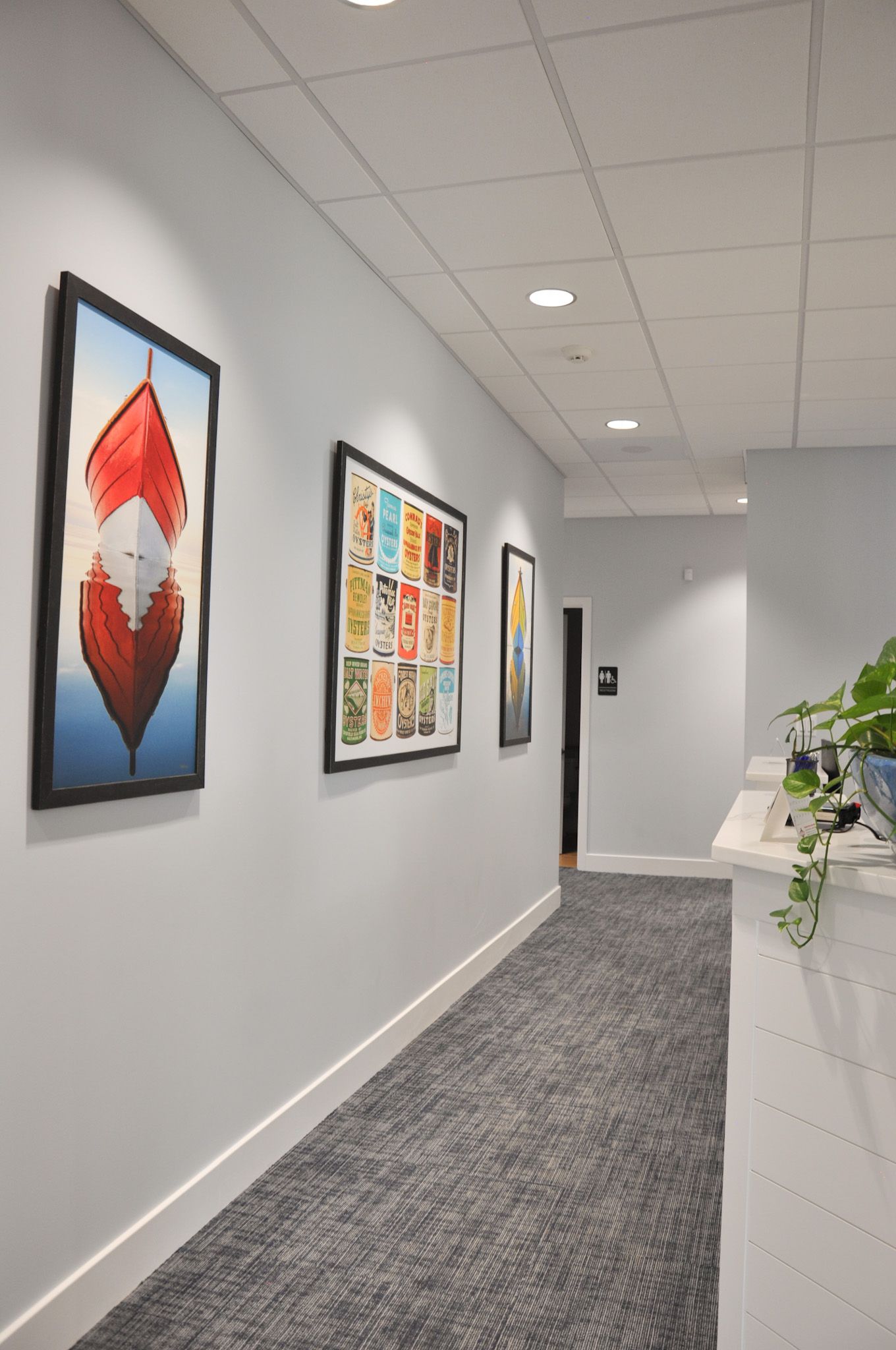 Narrow hallway with gray walls, artwork, and gray carpet. White trim and ceiling with recessed lighting.