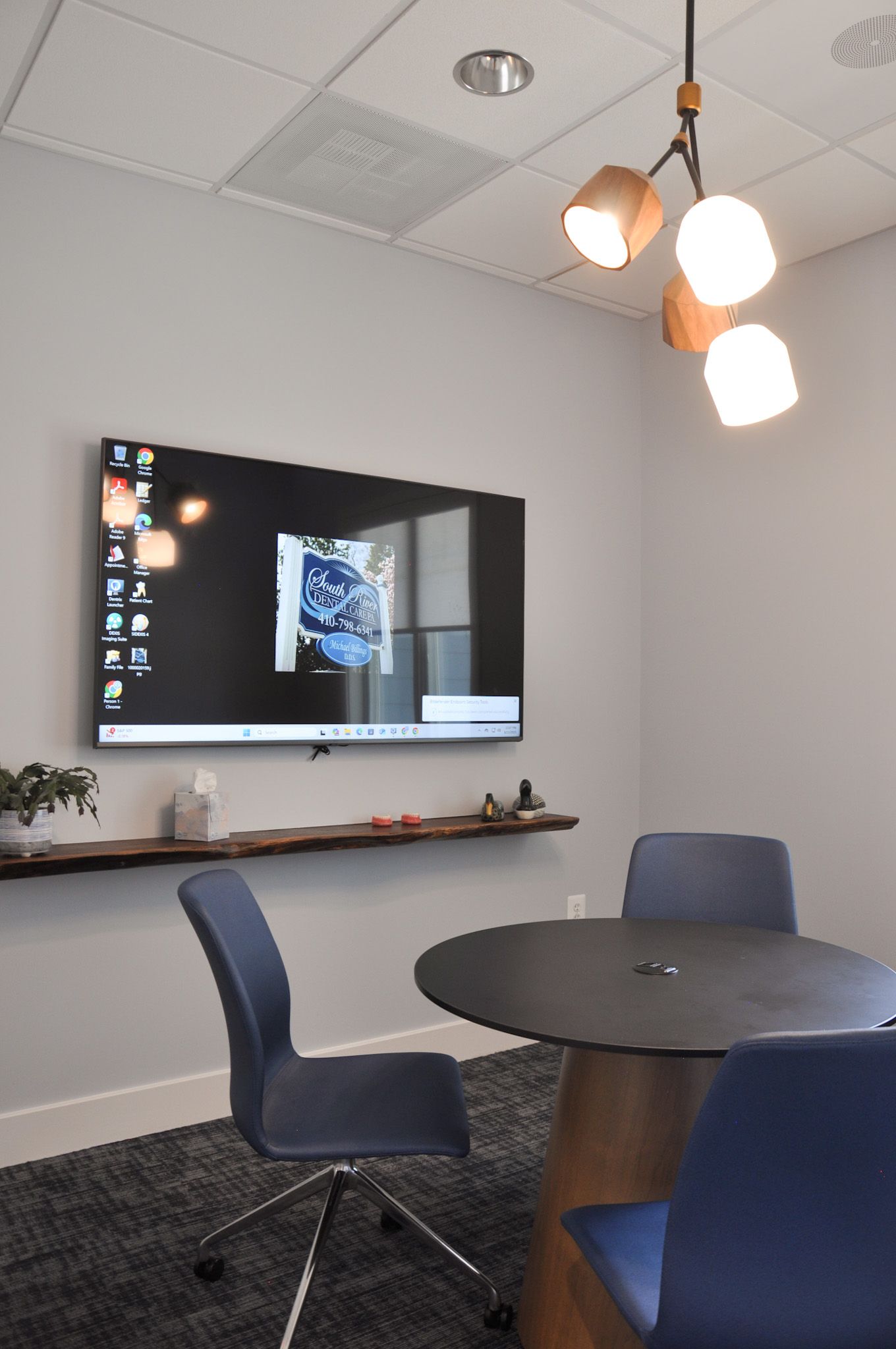 Conference room with a large TV, round table, blue chairs, and a unique light fixture.